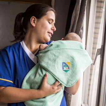 Verzorgster staat met baby aan raam